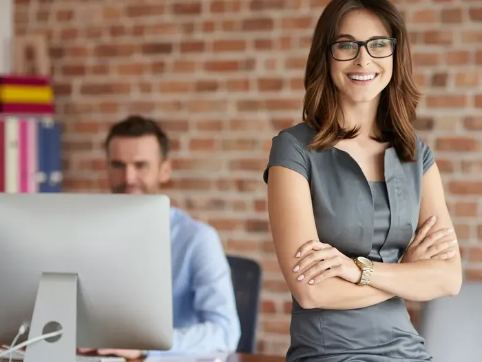 Smiling professional in a modern office, arms crossed near coworker at computer, representing Local Directory HQ